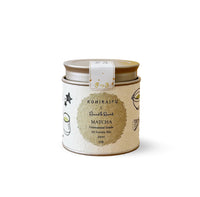 A round metal tin of Kohiraifu Matcha green tea, featuring a cream-colored label with a central gold circle and black text, topped with a gold lid and a white paper band.